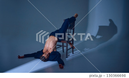 Male performer lying upside down on chair in dark suit with emotional vulnerability Male performer lying upside down on chair in dark suit with emotional vulnerability 130366698