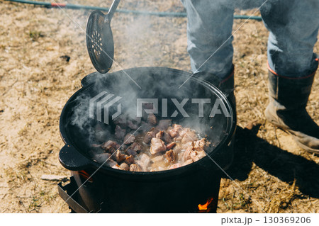 Meat cooking in a large cauldron outdoors over an open fire, a classic outdoor cooking concept for camping and traditional cuisine. 130369206