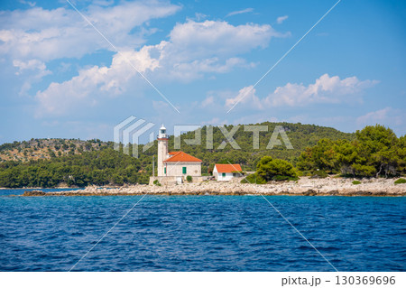 Stone lighthouse with red roof on the rocky coast of Hvar Island, Croatia, surrounded by pine trees and clear blue sea. Navigation, solitude and maritime heritage in the Adriatic. Stone lighthouse with red roof on the rocky coast of Hvar Island, Croatia, surrounded by pine trees and clear blue sea. Navigation, solitude and maritime heritage in the Adriatic. 130369696