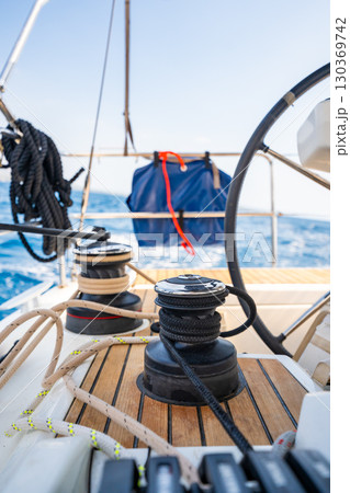 Cockpit of a sailing yacht with steering wheel, winches and ropes during navigation near Croatia. Sailing equipment, control and lifestyle at sea. Cockpit of a sailing yacht with steering wheel, winches and ropes during navigation near Croatia. Sailing equipment, control and lifestyle at sea. 130369742