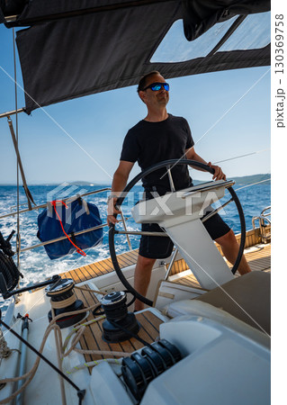 Man standing at the helm of a sailing yacht near Croatia, steering the boat through open water. Leadership, control, sailing lifestyle and freedom at sea. Man standing at the helm of a sailing yacht near Croatia, steering the boat through open water. Leadership, control, sailing lifestyle and freedom at sea. 130369758