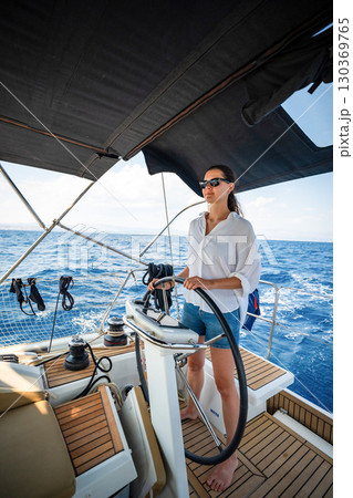 Young woman steering a sailing yacht near Croatia, confidently standing at the helm. Female leadership, empowerment and freedom in maritime lifestyle. 130369765