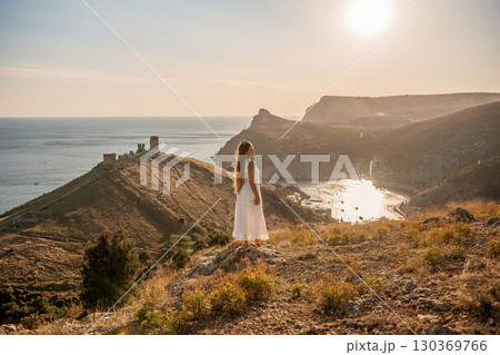 woman stands on a hill overlooking the ocean, her arms raised in the air. Concept of freedom and joy, as if the woman is celebrating a moment of happiness or accomplishment. woman stands on a hill overlooking the ocean, her arms raised in the air. Concept of freedom and joy, as if the woman is celebrating a moment of happiness or accomplishment. 130369766