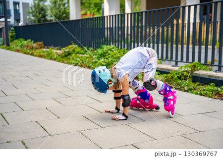 Little girl trying to stand up on roller skates after falling during her first attempts to skate. Persistence, physical development and learning through challenge in early childhood. Little girl trying to stand up on roller skates after falling during her first attempts to skate. Persistence, physical development and learning through challenge in early childhood. 130369767