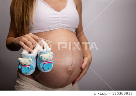 Pregnant woman holding blue baby shoes with little bears. Pregnant woman holding blue baby shoes with little bears. 130369915