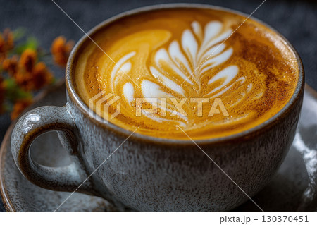 Steaming latte with intricate milk foam art in a ceramic cup 130370451