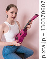 Young woman musician in positive light, holding ukulele. Her face conveys joy and she is looking at camera with sincere smile. Her positive facial expression conveys sense of cheer and friendliness 130370607