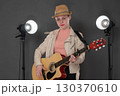 Young woman guitarist with classical six string acoustic guitar standing on stage, looking at camera. 18 year old female wearing eyeglasses. Serious musician is dressed in straw hat and beige jacket 130370610