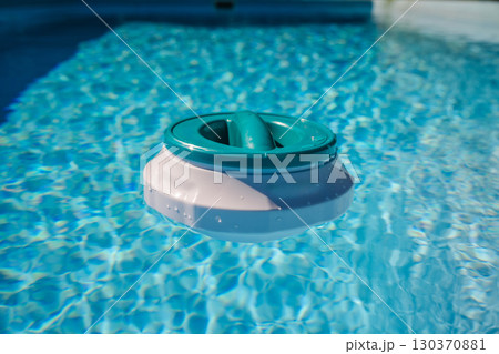 Floating pool chlorinator on clear blue water surface, used for chemical disinfection and regular pool care Floating pool chlorinator on clear blue water surface, used for chemical disinfection and regular pool care 130370881