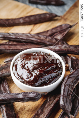 bowl of carob spread and pods on a wooden table 130371595