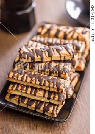 Sfogliatine glassate with chocolate. Italian crispy dessert on plate on wooden table. 130373042