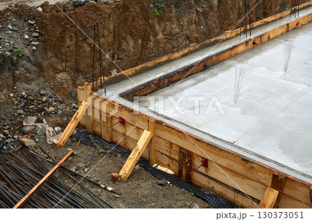 A concrete foundation is being poured on the construction site. Wooden formwork is used. 130373051