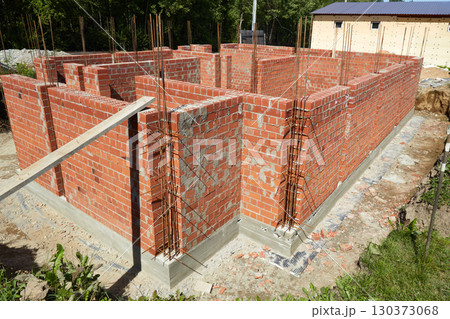 Brick walls are rising at a construction site, supported by wooden forms and metal rods. Brick walls are rising at a construction site, supported by wooden forms and metal rods. 130373068