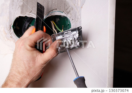 A person is using a screwdriver to install an electrical outlet on a white wall. 130373074