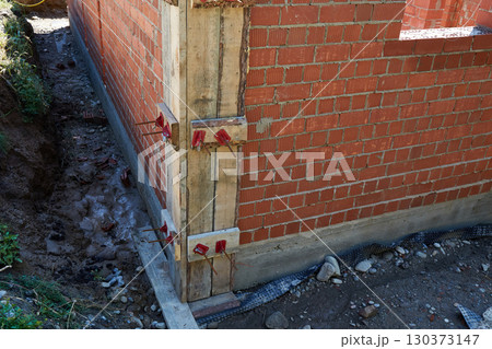 Brick walls are rising at a construction site, supported by wooden forms and metal rods. Brick walls are rising at a construction site, supported by wooden forms and metal rods. 130373147