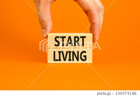 Start living symbol. Concept words Start living on beautiful wooden block. Beautiful orange table orange background. Businessman hand. Business and Start living concept. Copy space. Start living symbol. Concept words Start living on beautiful wooden block. Beautiful orange table orange background. Businessman hand. Business and Start living concept. Copy space. 130373186