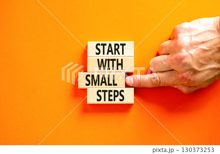 Start with small steps symbol. Concept words phrase Start with small steps on beautiful wooden blocks. Beautiful orange background. Businessman hand Business Start with small steps concept. Copy space 130373253