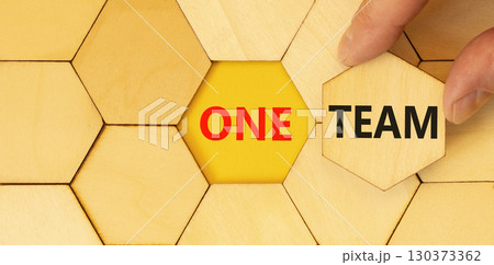 One team symbol. Concept word One team on beautiful wooden puzzles. Businessman's hand. Beautiful yellow paper background. Business one team concept. Copy space. One team symbol. Concept word One team on beautiful wooden puzzles. Businessman's hand. Beautiful yellow paper background. Business one team concept. Copy space. 130373362