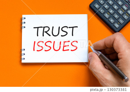 Trust issues symbol. Concept word Trust issues on beautiful white note. Businessman's hand. Black calculator. Beautiful orange paper background. Business trust issues concept. Copy space. 130373381