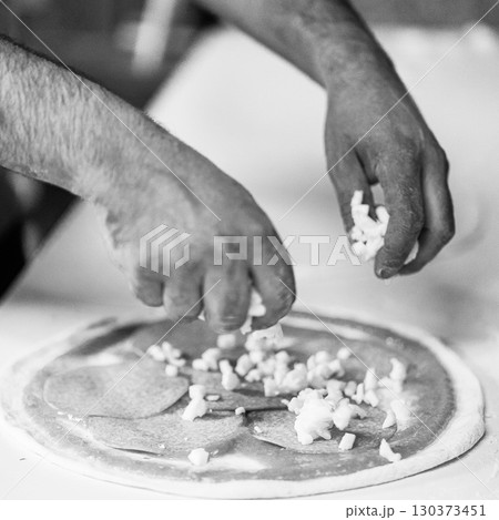 Hands preparing a pizza putting salami on pizza 130373451