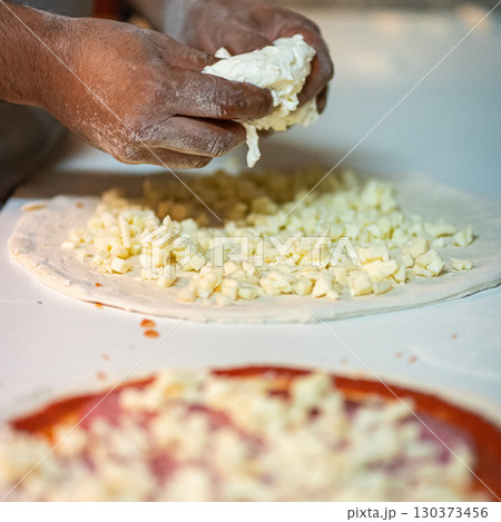 Hands preparing a pizza putting cheese mozzarella on pizza 130373456