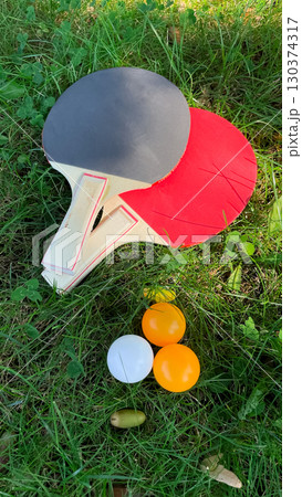 Table tennis rackets and balls on green grass, outdoor leisure 130374317