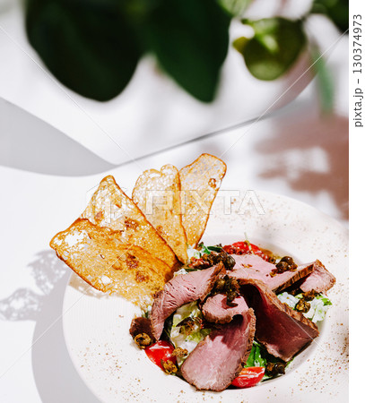 Delicious plate with roast beef, salad, and crispy chips on a white table 130374973