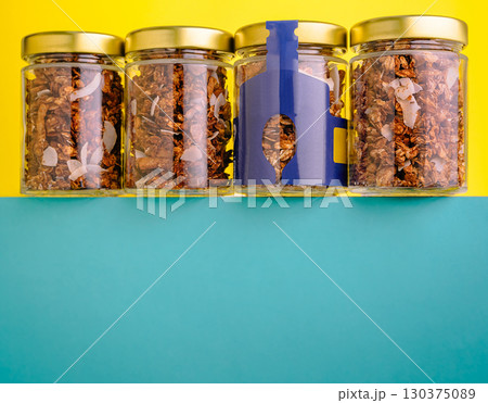 Glass jars with granola and coconut flakes on colorful background 130375089
