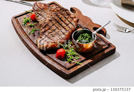 Large grilled steak served on a wooden board with herbs and sauce 130375137