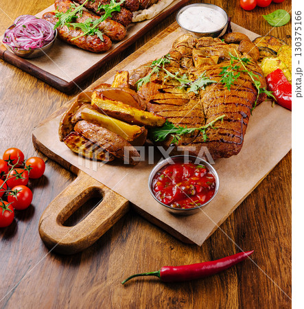 Sizzling platter of grilled meats and vegetables served on a wooden board Sizzling platter of grilled meats and vegetables served on a wooden board 130375166