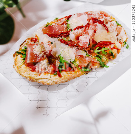 Delicious flatbread with prosciutto and arugula at a cozy restaurant Delicious flatbread with prosciutto and arugula at a cozy restaurant 130375243