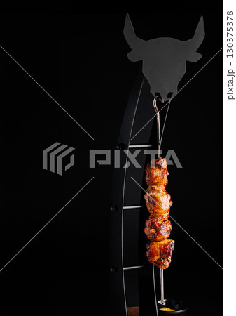 Delicious meat skewer hanging on artistic grill display in dark setting 130375378