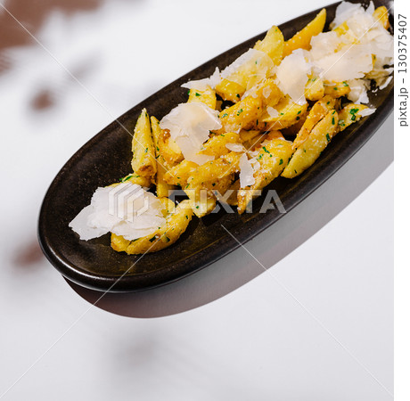 Crispy seasoned potato fries topped with cheese on a sleek black plate Crispy seasoned potato fries topped with cheese on a sleek black plate 130375407