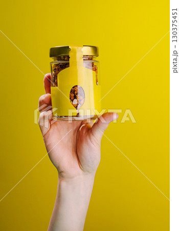 Hand holding a jar of granola against a bright yellow background 130375451