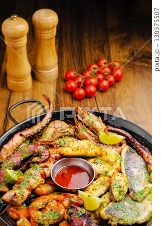 Seafood platter featuring grilled shrimp, fish, and vegetables on wooden table 130375507