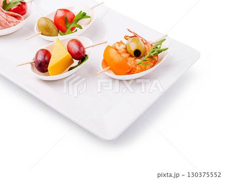 Variety of appetizer skewers displayed on a white platter at a gathering 130375552