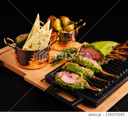 Deliciously prepared lamb rack with green herb crust and sides 130375565