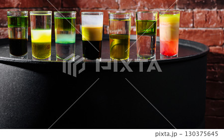 Colorful shots arranged on a black table with a brick backdrop at a bar 130375645