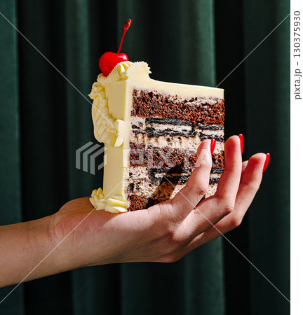 Hand holding a delicious layered cake topped with cherry Hand holding a delicious layered cake topped with cherry 130375930