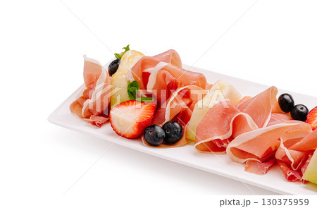 Platter of prosciutto, fresh fruits, and mint leaves displayed artfully 130375959