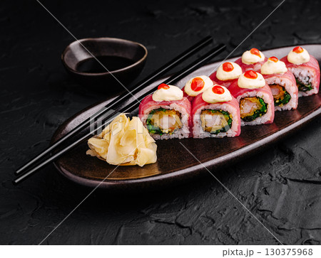 Delicious sushi rolls presented on a dark plate with garnishes and soy sauce 130375968