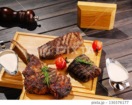 Delicious grilled meats served on wooden platter with garnish and sauce Delicious grilled meats served on wooden platter with garnish and sauce 130376177
