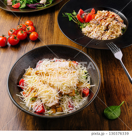 Delicious salad bowls with fresh tomatoes on a wooden table setting 130376339