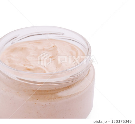 Glass jar filled with creamy light beige sauce or dip, smooth texture, isolated on white background 130376349