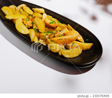 Crispy golden potato wedges garnished with herbs on a black serving dish Crispy golden potato wedges garnished with herbs on a black serving dish 130376409