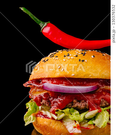 Delicious burger topped with chili pepper served against a black backdrop 130376532