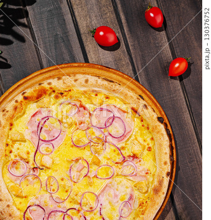 Delicious pizza with ham, onion, and cherry tomatoes on a wooden table 130376752