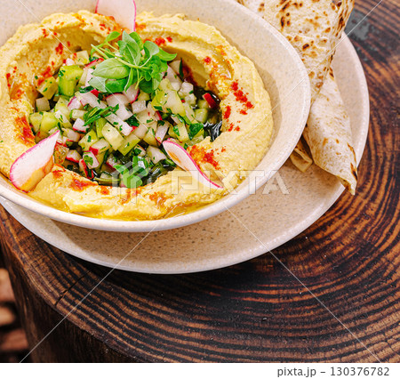 Delicious hummus topped with fresh vegetables served with flatbread Delicious hummus topped with fresh vegetables served with flatbread 130376782