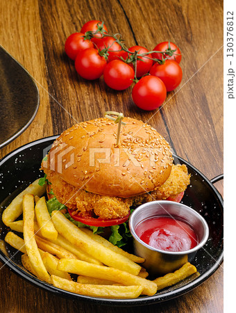 Crispy chicken burger with fries and fresh tomatoes on wooden table 130376812