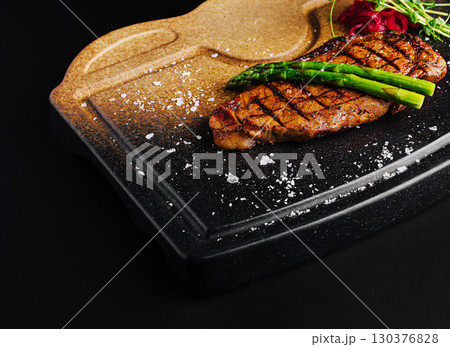 Grilled steak served on a black stone platter with asparagus and seasoning Grilled steak served on a black stone platter with asparagus and seasoning 130376828
